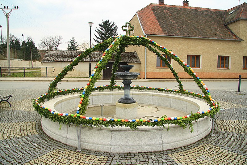 Ein Brunnen, der mit einer Krone aus grünen Zweigen mit Ostereiern verziehrt ist.