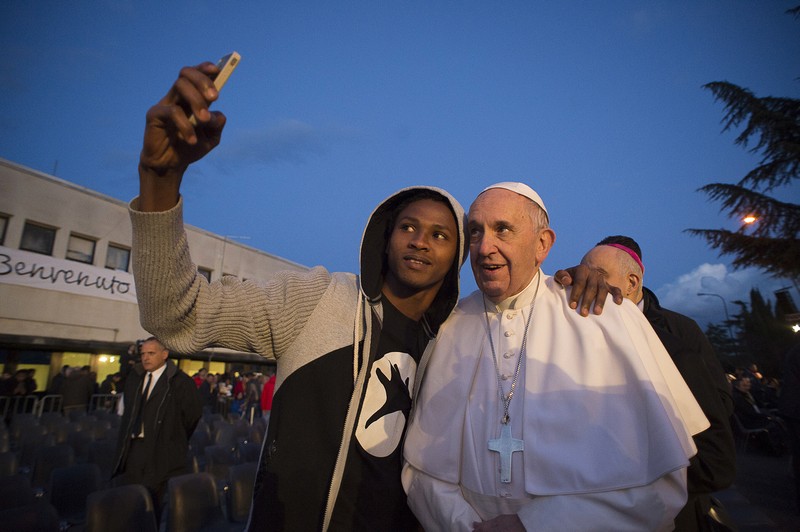 Ein Migrant macht ein Selfie mit Papst Franziskus.