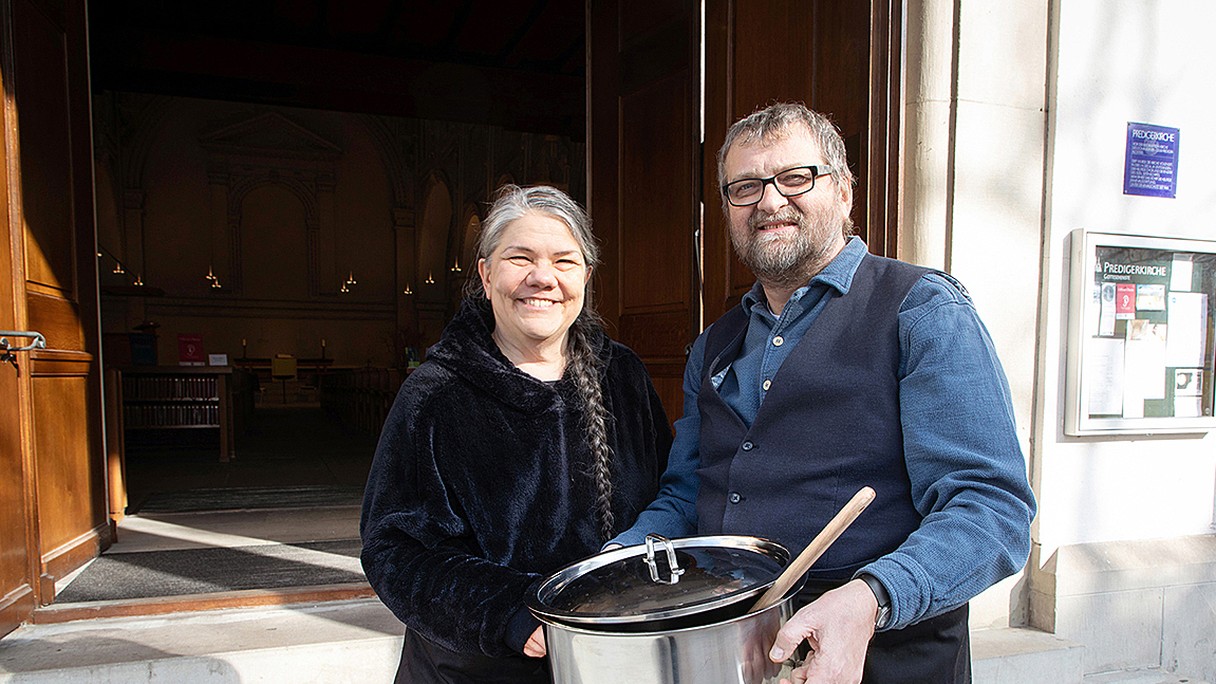 Thomas Münch und Belinda Harris stehen mit einem grossen Kochtopf vor der Predigerkirche