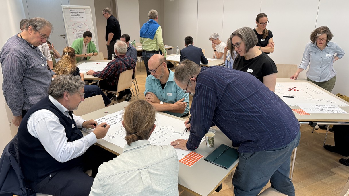 Eine Gruppe Menschen erarbeiten an Tischen auf grossen Papierbögen Ideen für eine bedürfnisorientierte Kirche