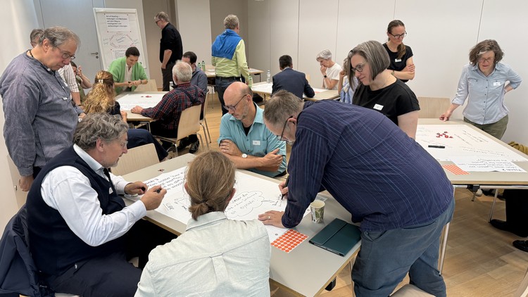 Eine Gruppe Menschen erarbeiten an Tischen auf grossen Papierbögen Ideen für eine bedürfnisorientierte Kirche
