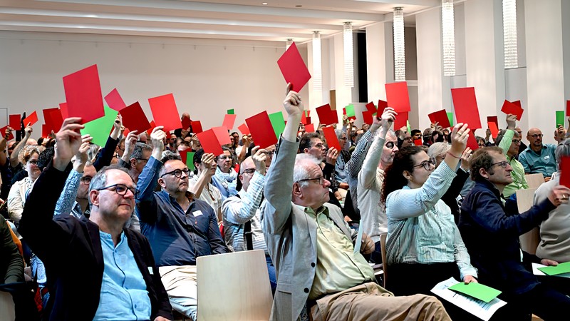 Rund 140 Teilnehmende halten rote und grüne Papiere in die Luft, um ihre Meinung kundzutun.