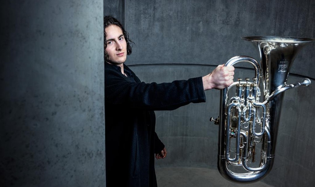 Klassik-Nachwuchsmusiker Valerian Alfaré mit seinem Instrument in Raum mit Betonwänden. Er streckt das Euphonium, ein Blechblasinstrument, von sich.