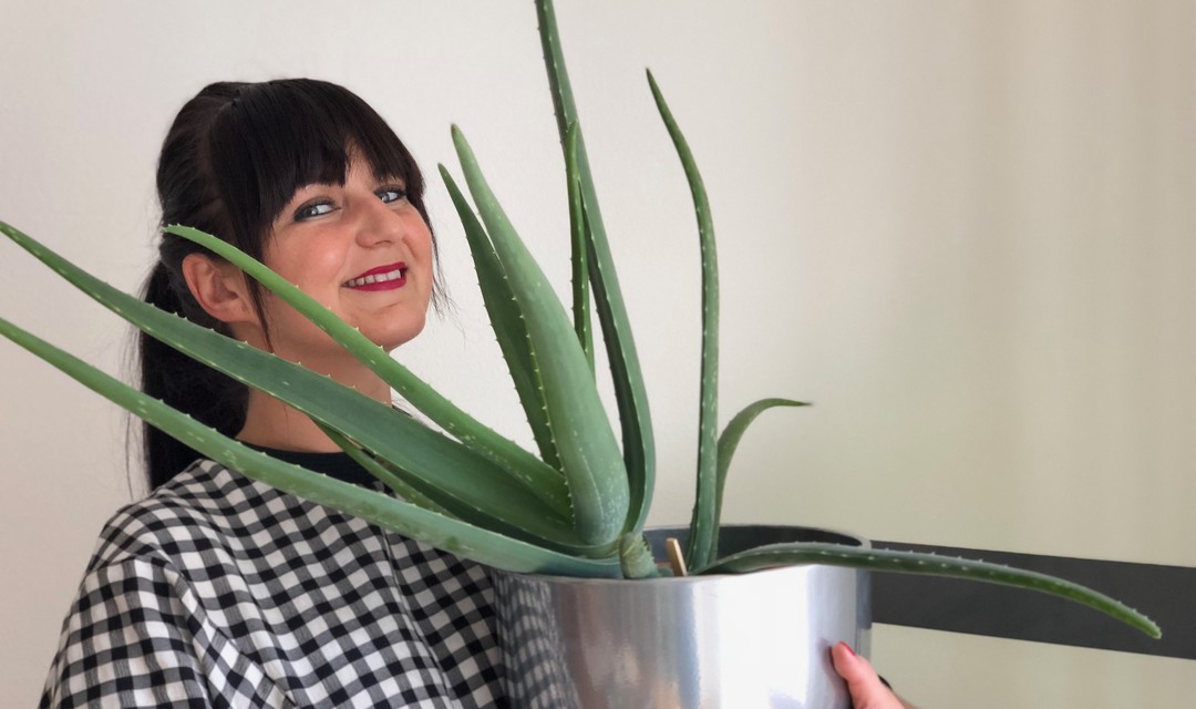 Ágota Dimén mit langen schwarzen Haaren und einer Pflanze vor dem Gesicht