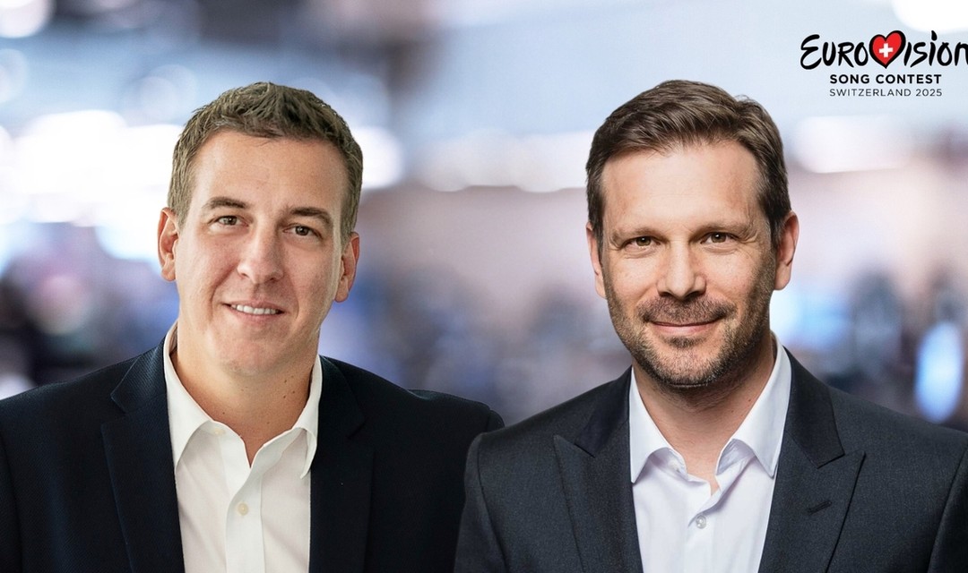 Reto Peritz und Moritz Stadler, frontal fotografiert mit unscharfem Hintergrund, das ESC 2025 Logo oben rechts