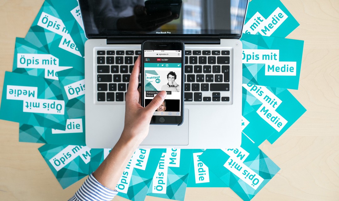 Hand hält Handy vor Laptop-Bildschirm