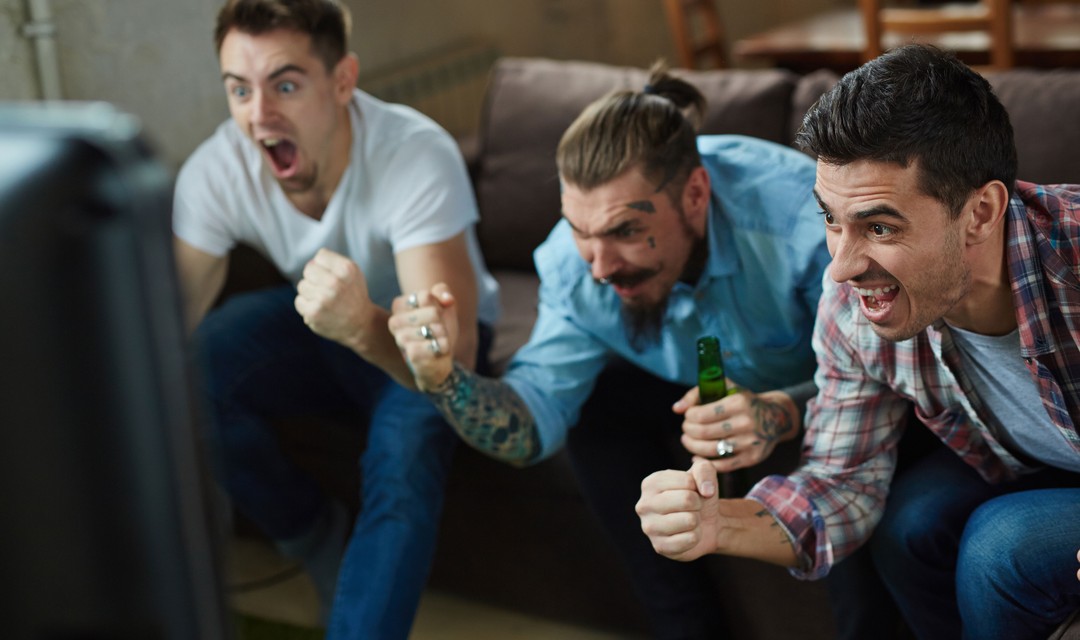 Junge Männer mit Bier jubeln vor dem TV.