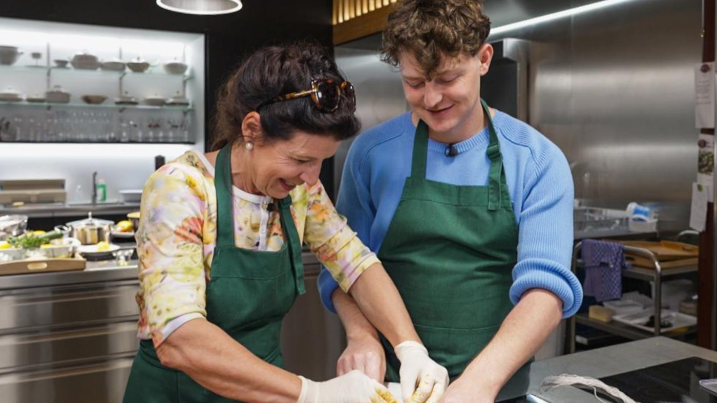 Frau und Mann (Mutter und Sohn?) kochen gemeinsam, beide mit grüner Schürze