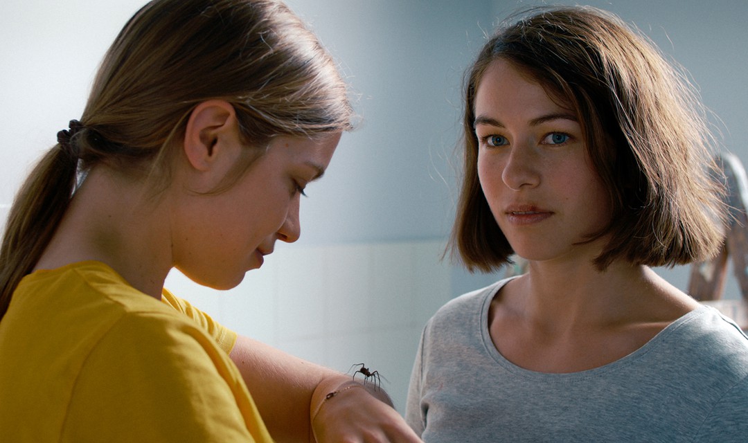 Zwei Frauen im Bild, eine mit einer Spinne auf dem Arm.