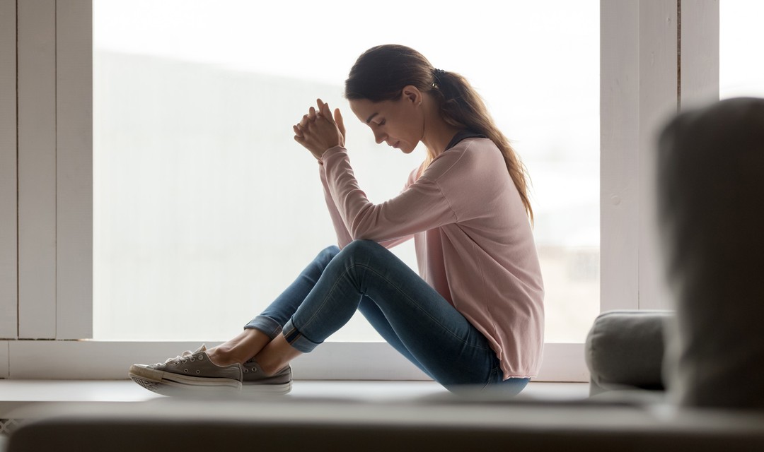 Eine Frau sitzt nachdenklich auf dem Fensterbrett und schaut nach draussen
