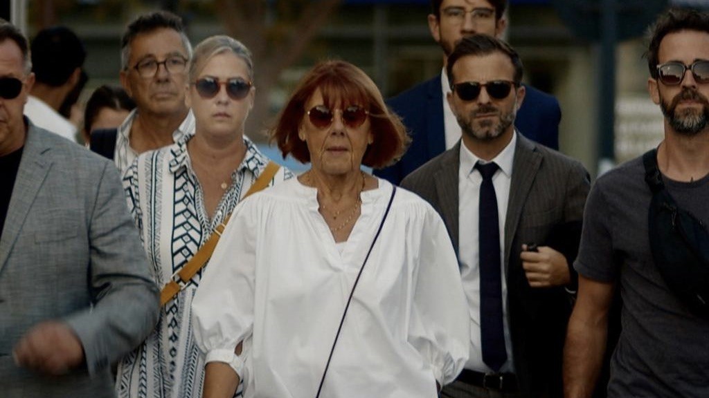 Gisèle Pelicot mit Sonnenbrille, mit mehreren anderen Menschen, läuft auf die Kamera zu