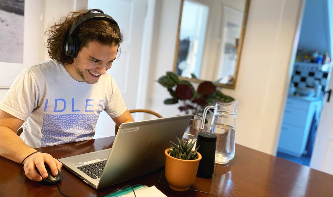 Jan sitzt in seiner Wohnung am Tisch mit Computer und Unterlagen.