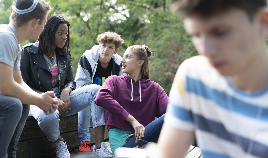 Jugendliche verschiedener Religionen und Hautfarbe sitzen zusammen auf einer Treppe