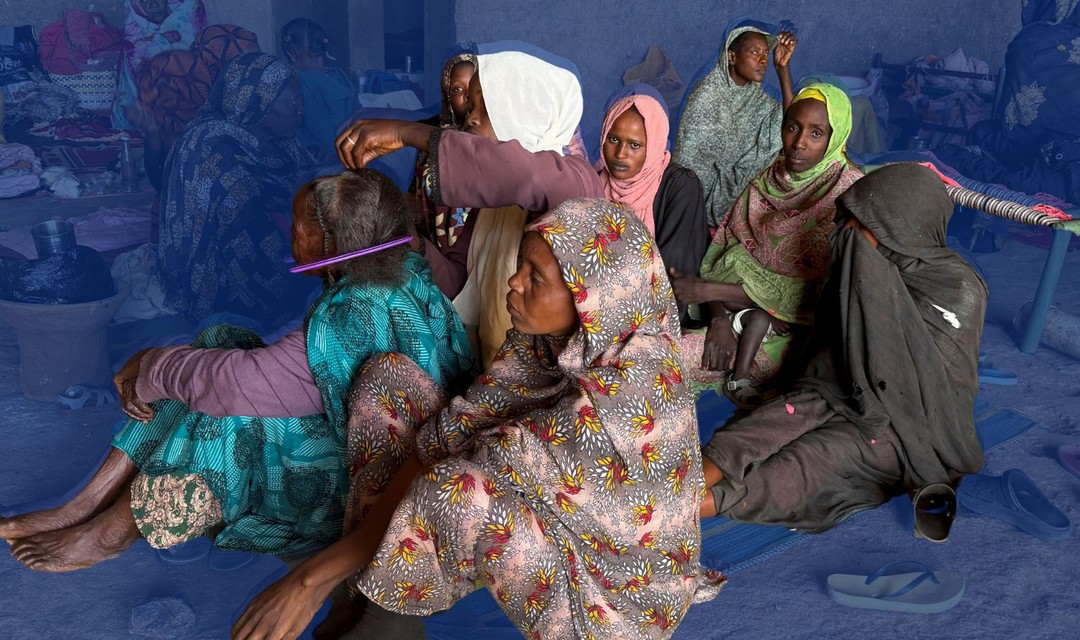 Das Foto zeigt vertriebene Frauen im Sudan in bunte Tuchkleider gehüllt. Sie sitzen am Boden in einem Registrierungszentrum.