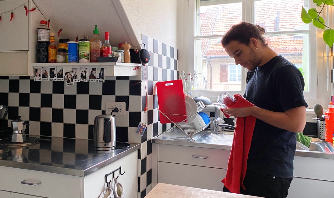 Jan steht zuhause in seiner Küche und trocknet ein Cocktailglas ab