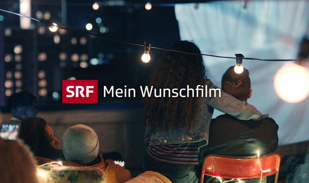 Lichterkette im Vordergrund, man sieht sitzende Menschen, die auf eine selbstgemachte Leinwand schauen, es ist Nacht, die Leinwand ist ein Bettlaken