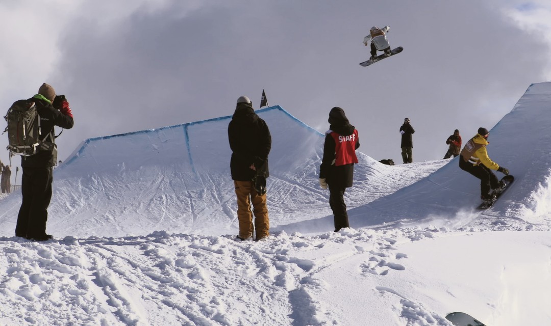 Giulia sitzt mit einem Snowboard an den Füssen im Schnee und wird dabei von Larissa gefilmt