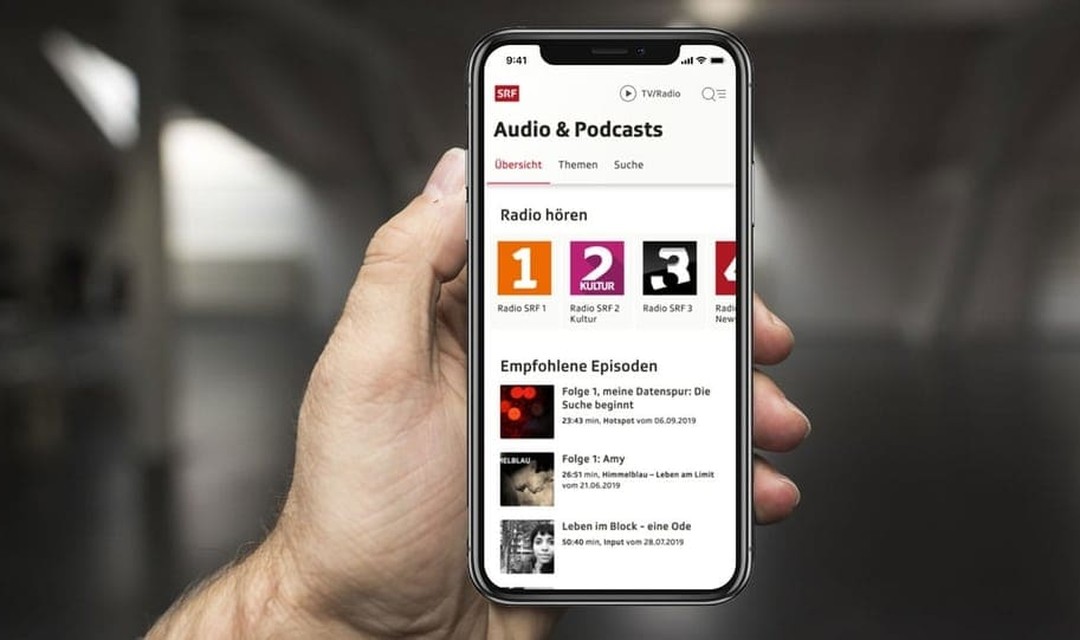 Hand hält ein Mobiltelefon, darauf ist die neue Audioplattform von SRF abgebildet