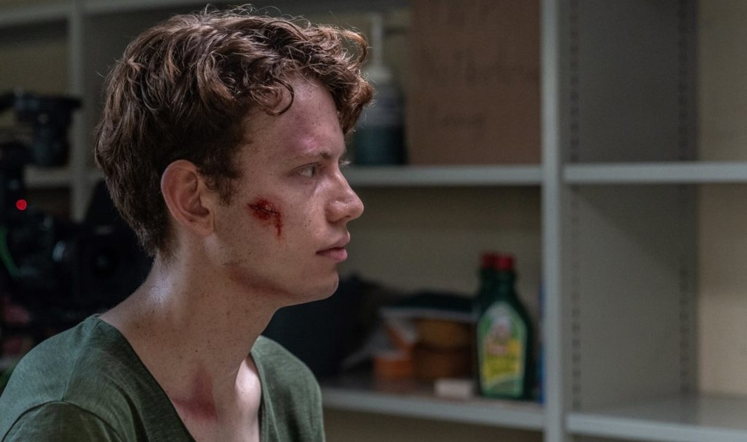 Ein Protagonist steht im Bunker, auf seiner Wange klafft eine grosse Wunde.