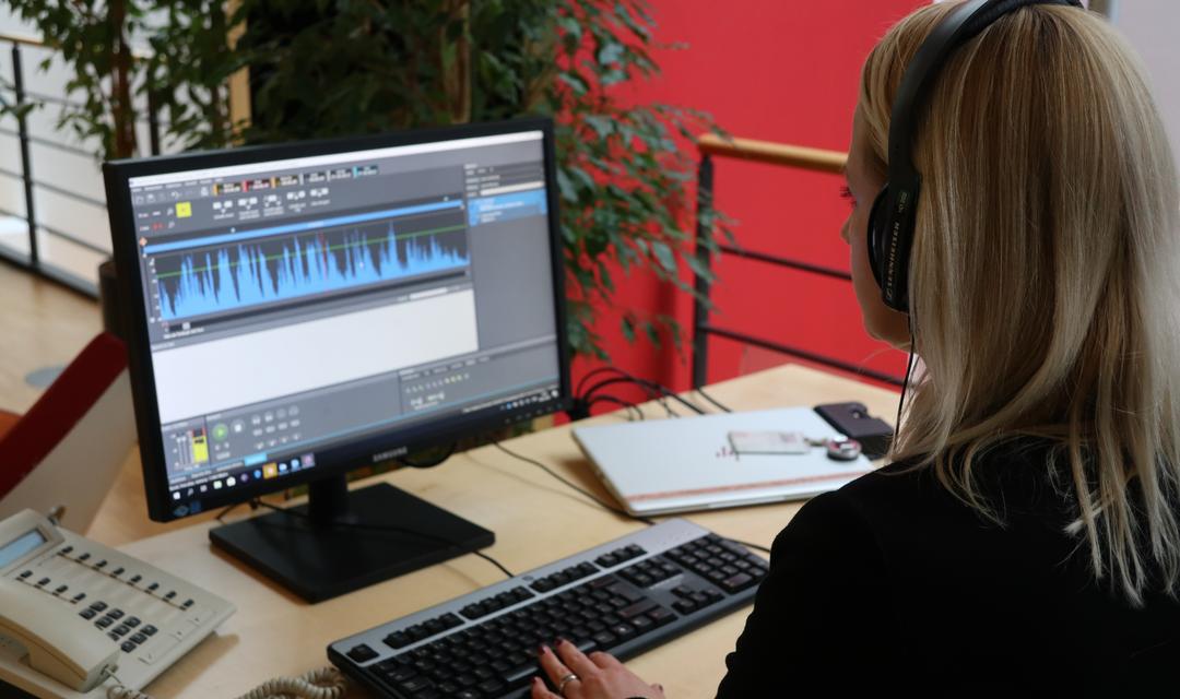 Isabelle Maissen sitzt mit Kopfhörern am Arbeitsplatz und schneidet den Podcast
